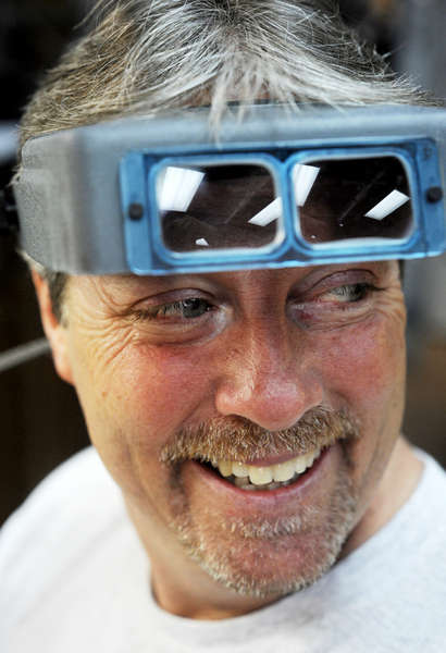 Tim Stoll, 51, smiles back at Angela during an exchange of jokes at the shop. He uses his goggles to examine jewelry.