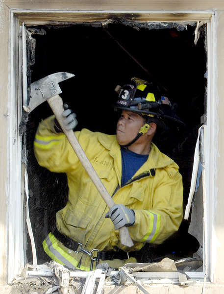 A San Jose firefighter cleans up a wrecked window after a fire destroyed part of the house. 