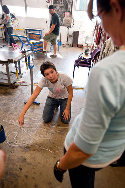 Beginning glassblowing students taking instruction on using wax and clay to mold glass objects.