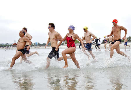 Participants of the swim master triathlon race to the water.